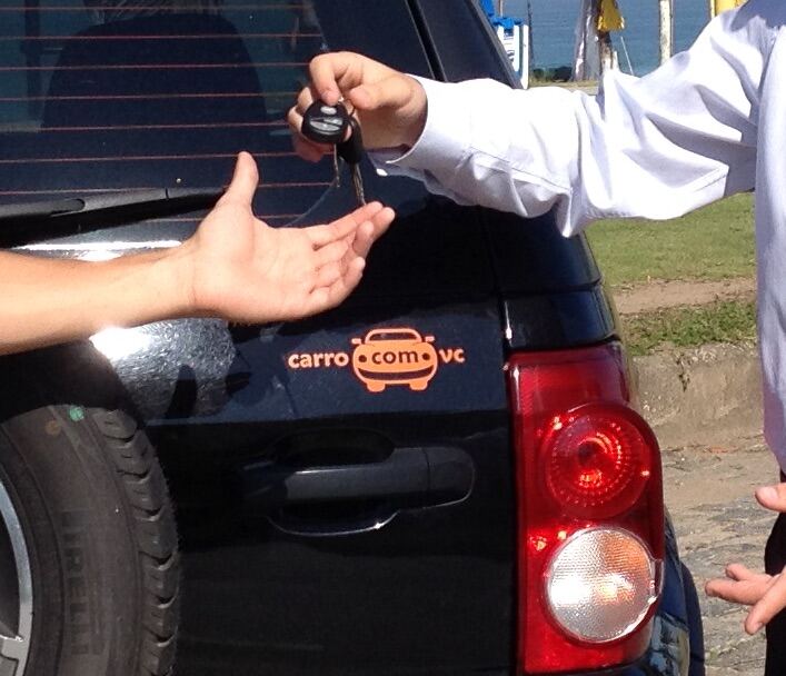 Handing over car keys next to a carro.com.vc sticker on a black car