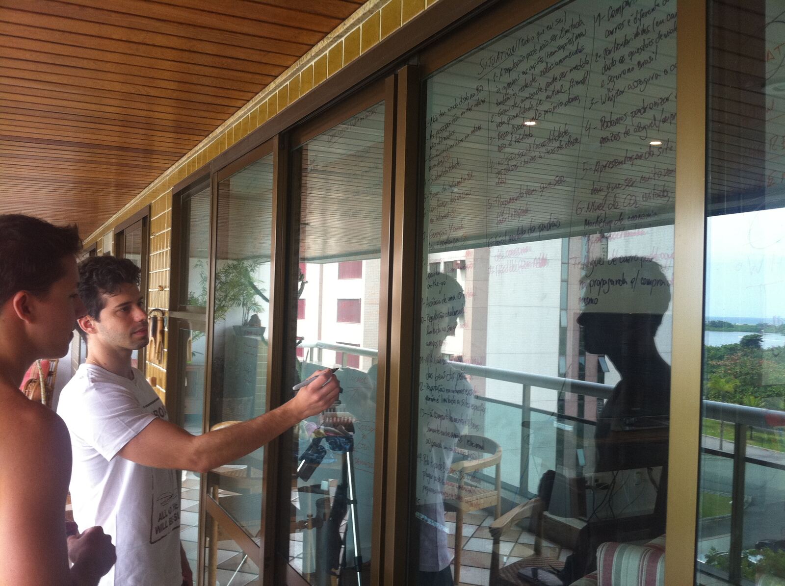Porto and Gustavo writing product ideas all over the glass windows of an apartment